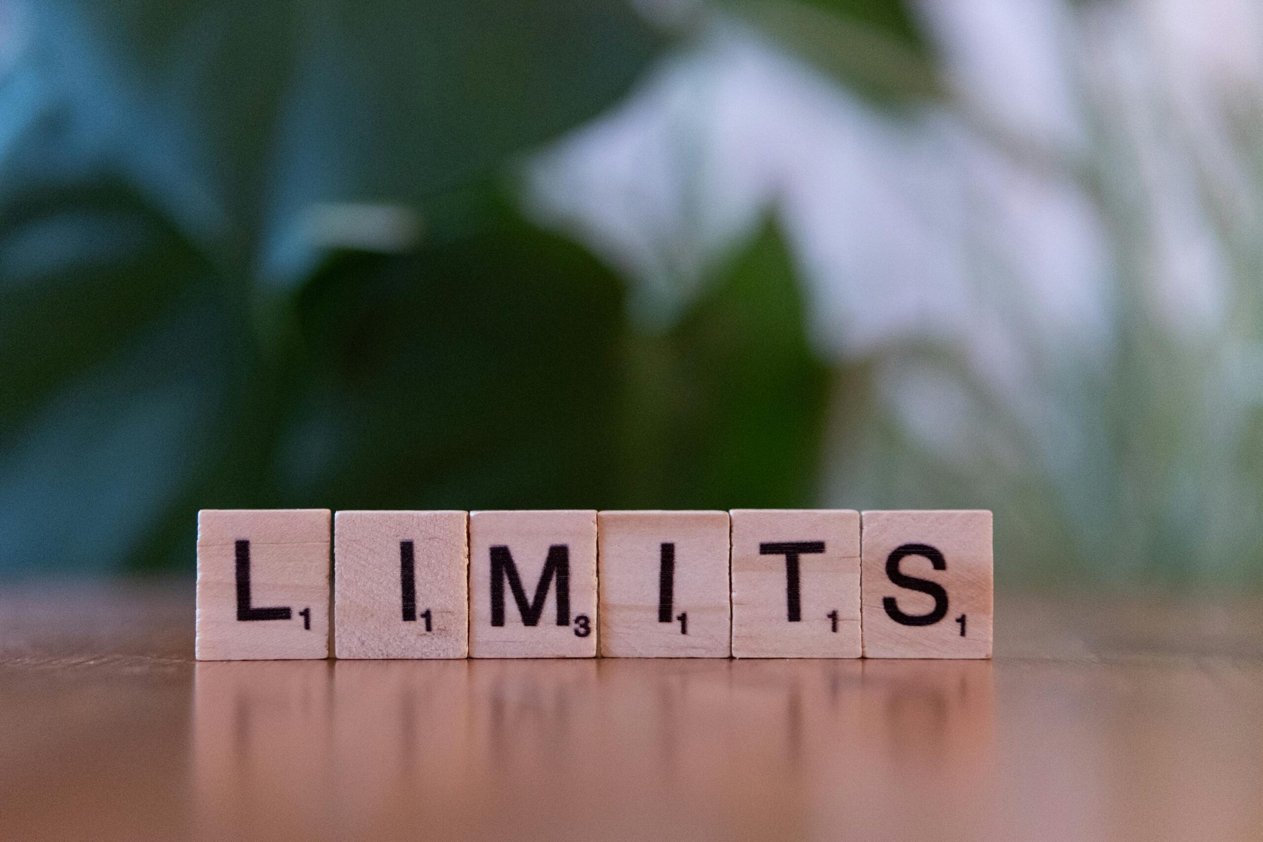 Wooden letter tiles forming the word 'LIMITS' on a wooden table.